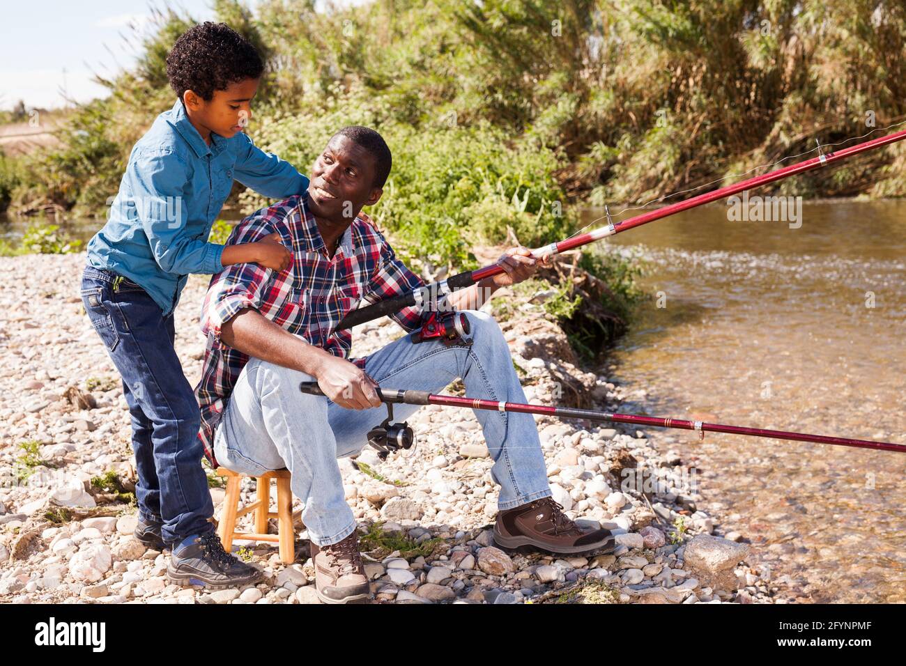 Portrait of fishermen - African boy and his father fishing with rods on river Stock Photo