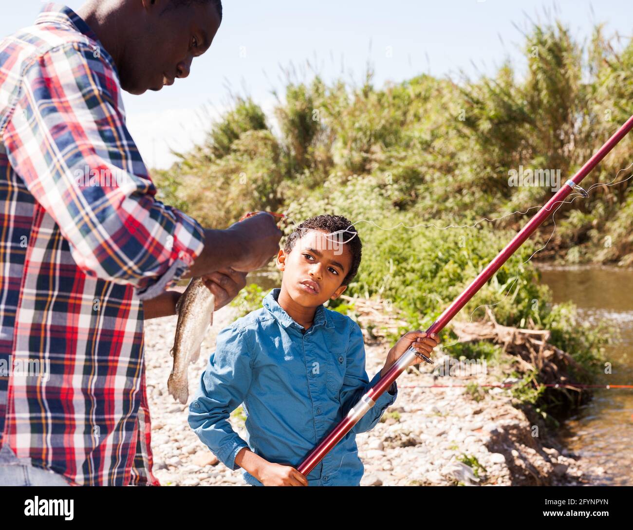 Portrait of enthusiastic little African boy and his father holding fishing rod with fish on hook Stock Photo