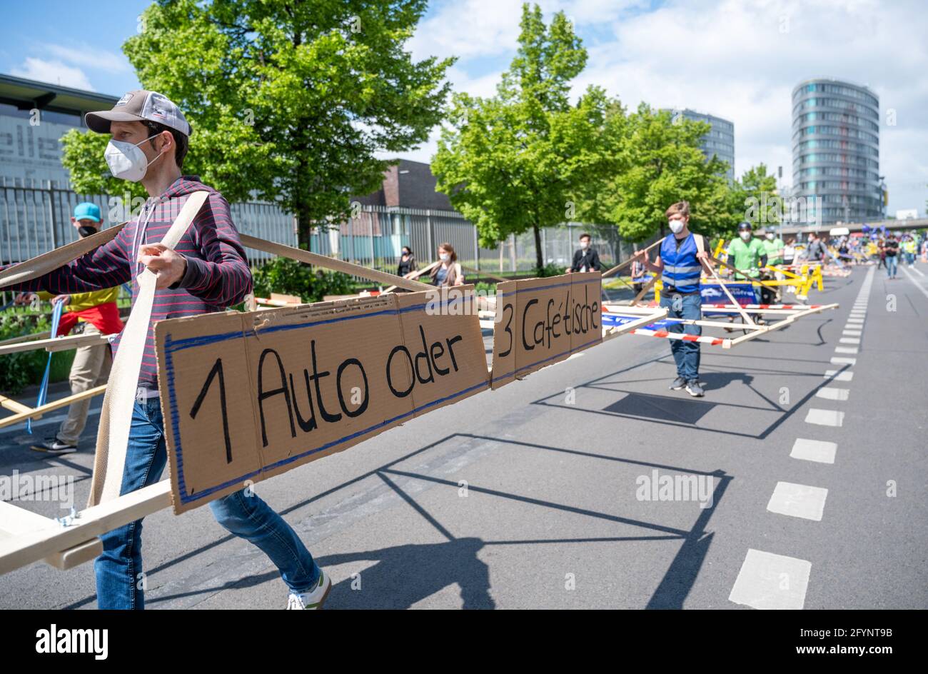 Berlin, Germany. 29th May, 2021. A participant carries a poster with the inscription '1 car or 3 café tables' during an action of 'Volksentscheid Berlin autofrei' and Greenpeace Berlin. During the action, wooden racks, which are supposed to represent the average space consumption of cars, are used to demonstrate against land consumption by cars. Credit: Christophe Gateau/dpa/Alamy Live News Stock Photo
