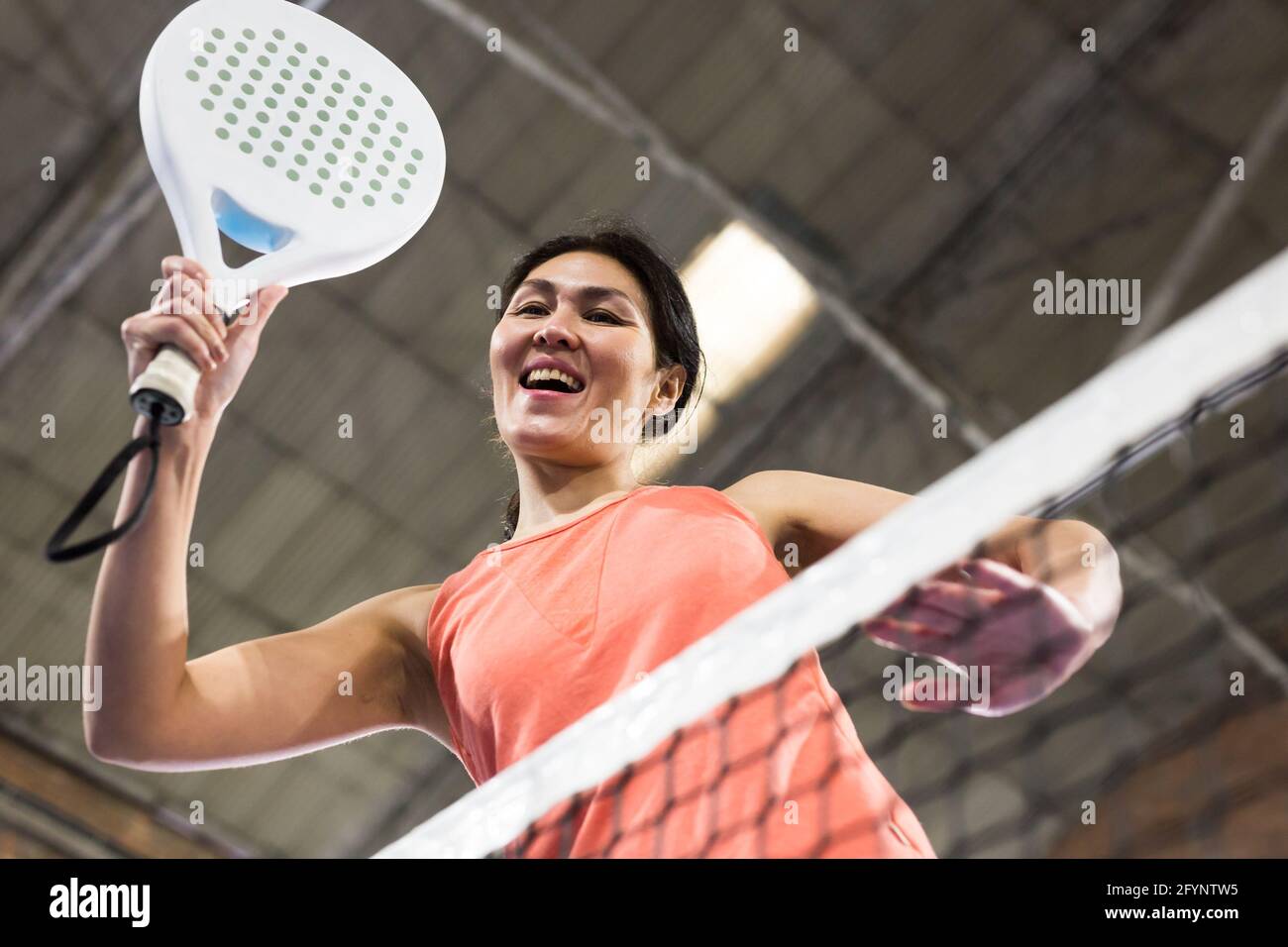 Portrait of emotional determined asian woman playing padel tennis, swinging her racket to return ball over net with forehand. Female player ready to h Stock Photo
