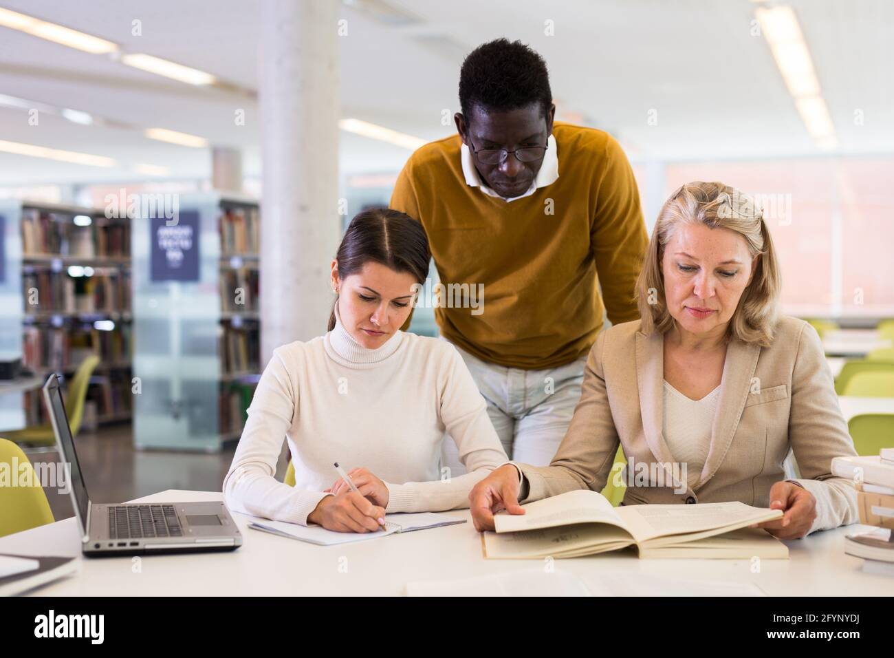 Female tutor helping students preparing for exam in library Stock Photo ...