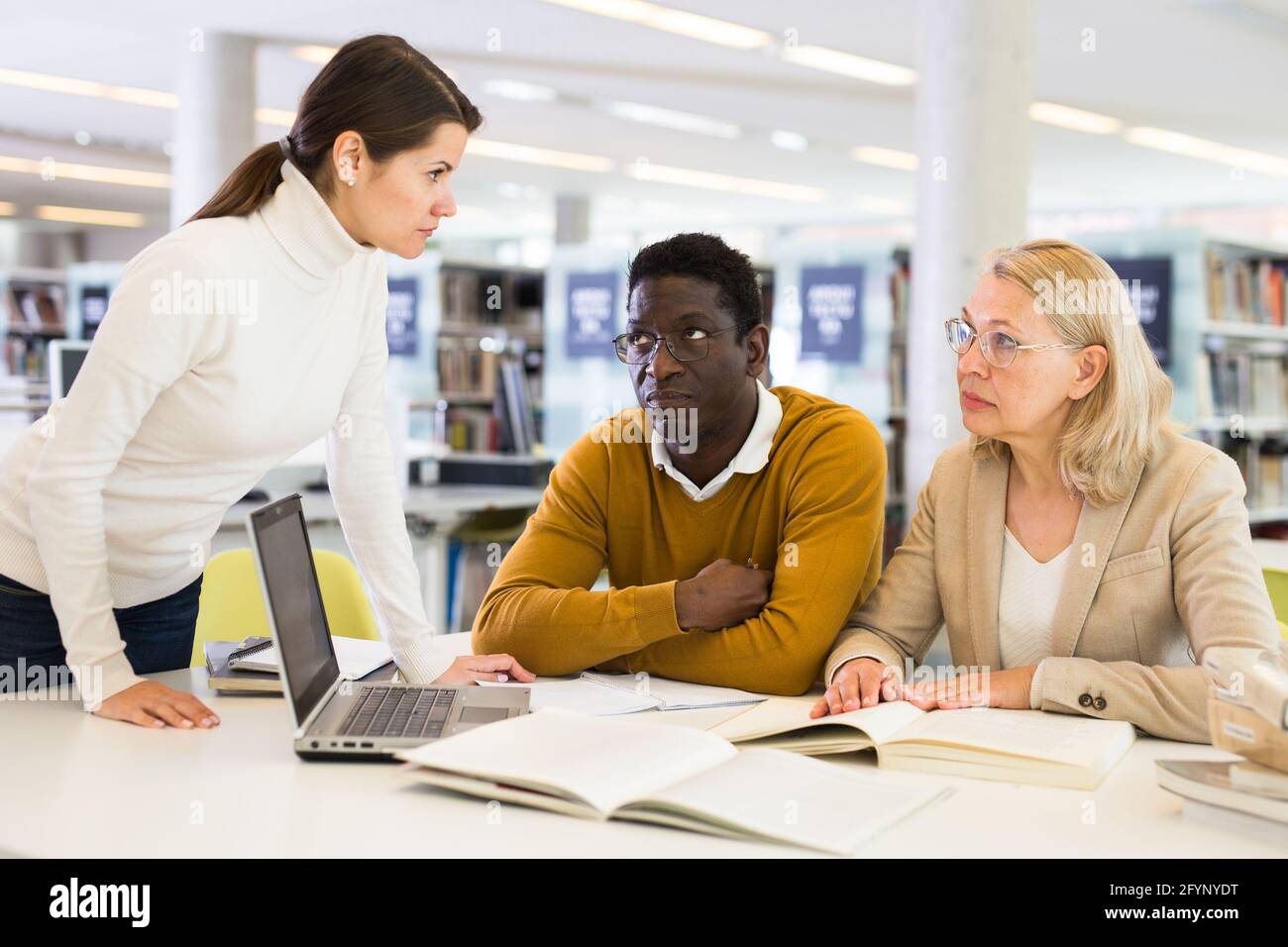 Female tutor helping students preparing for exam in library Stock Photo ...