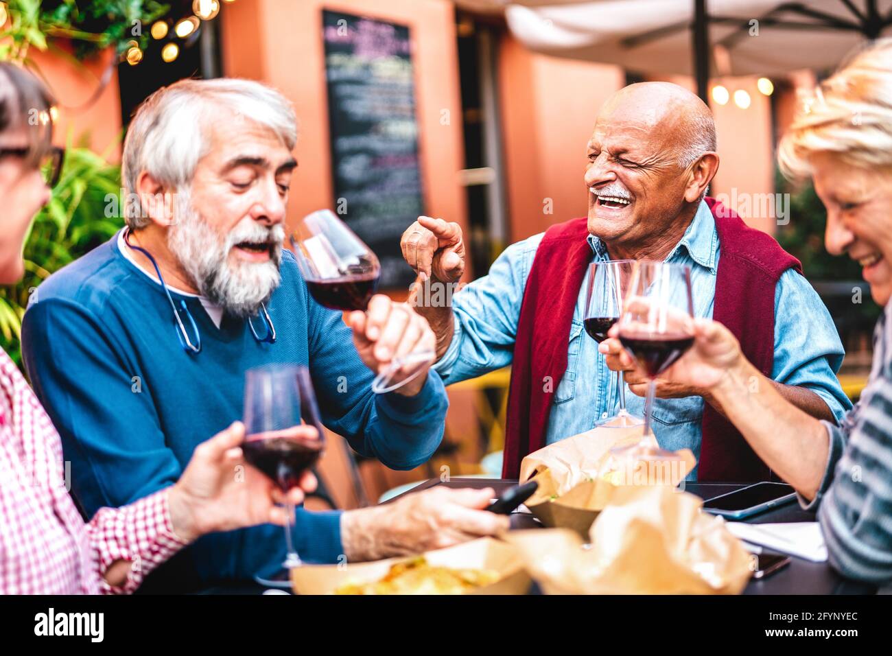 Happy retired friends having fun drinking red wine at pre dinner party - Senior people eating at restaurant together - Dinning life style concept Stock Photo