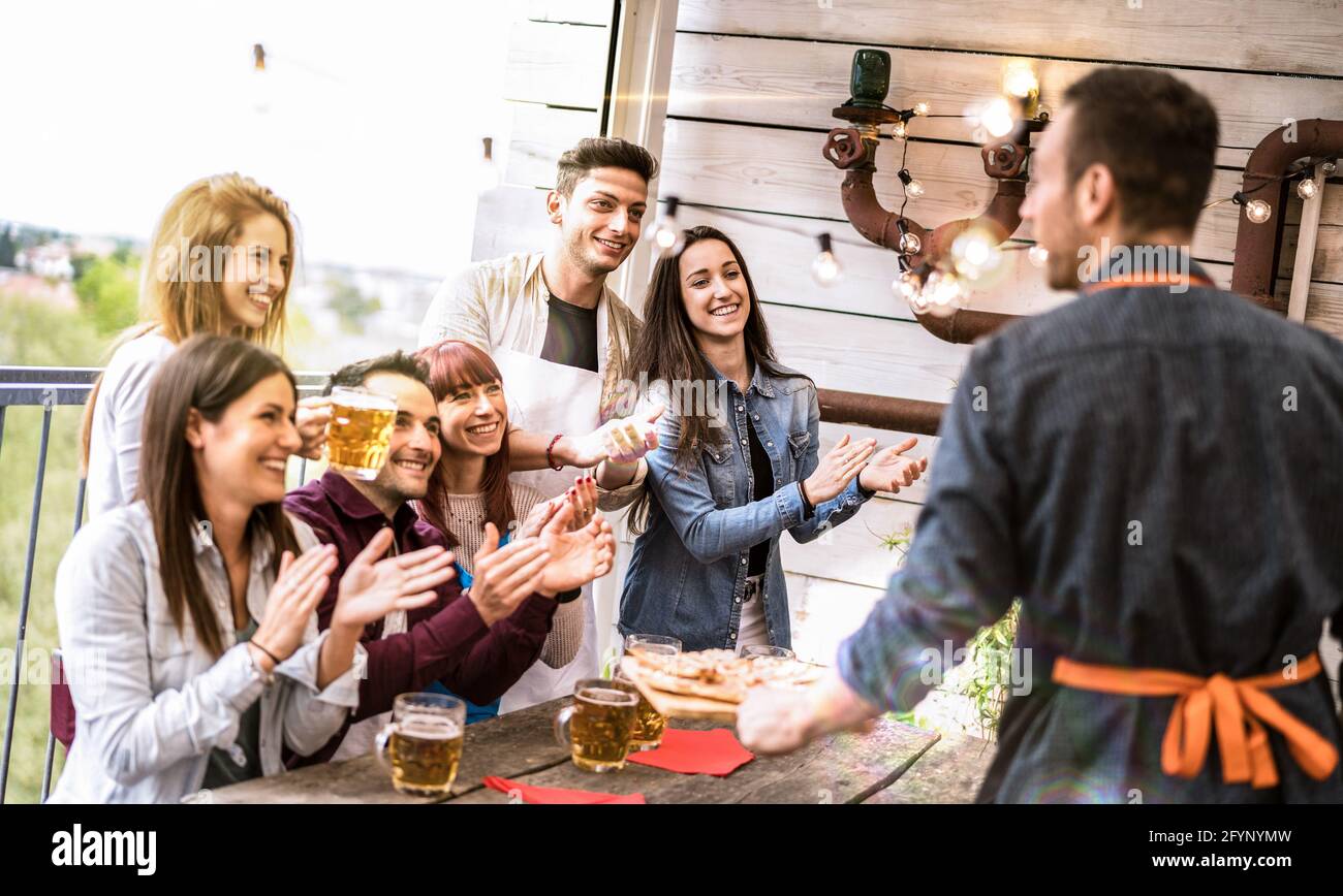 Young friends having fun drinking beer on balcony at house dinner party - Happy people eating pizza at fancy alternative restaurant together Stock Photo