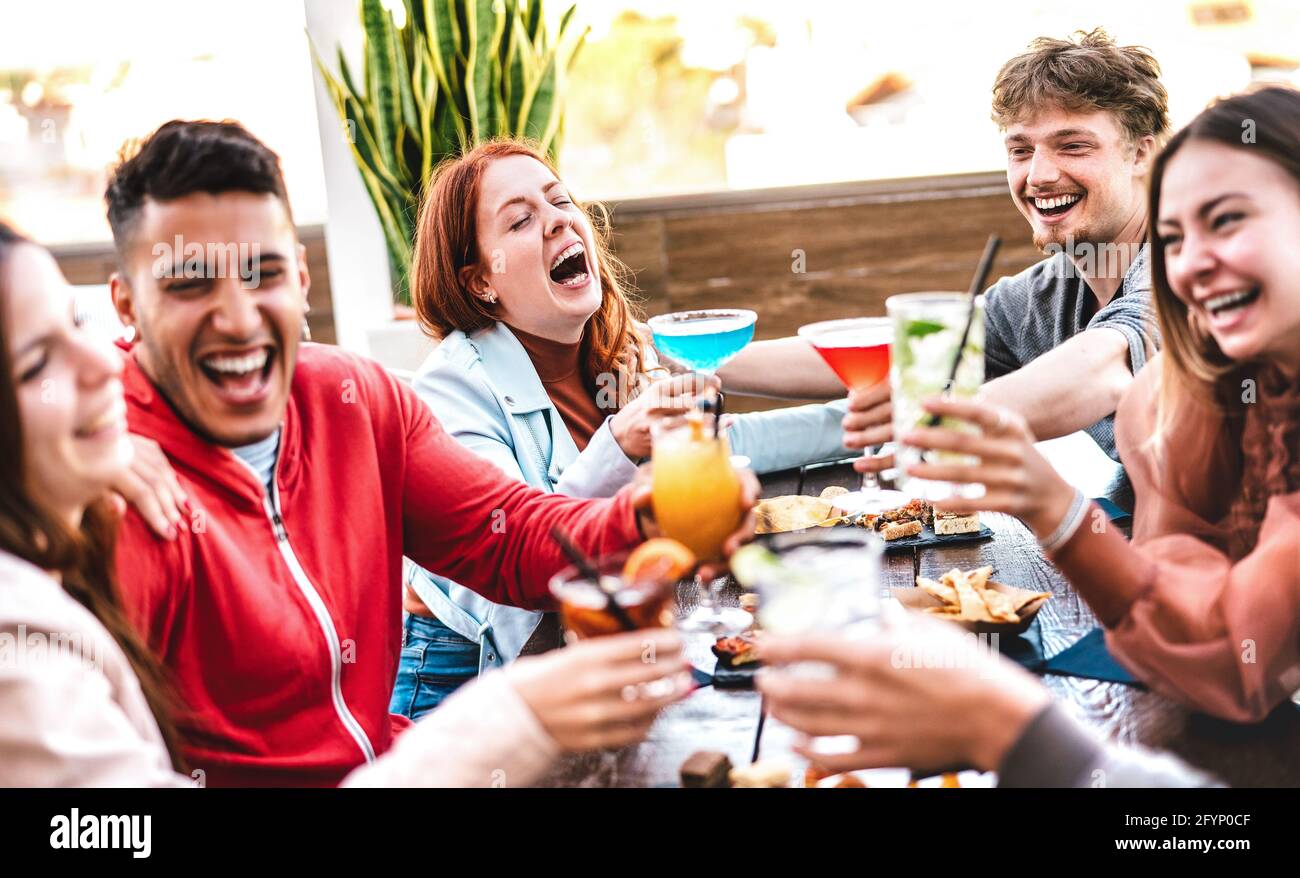 Friends toasting multicolored drinks at open air bar restaurant after work - Life style concept with people having fun together sharing cocktails Stock Photo