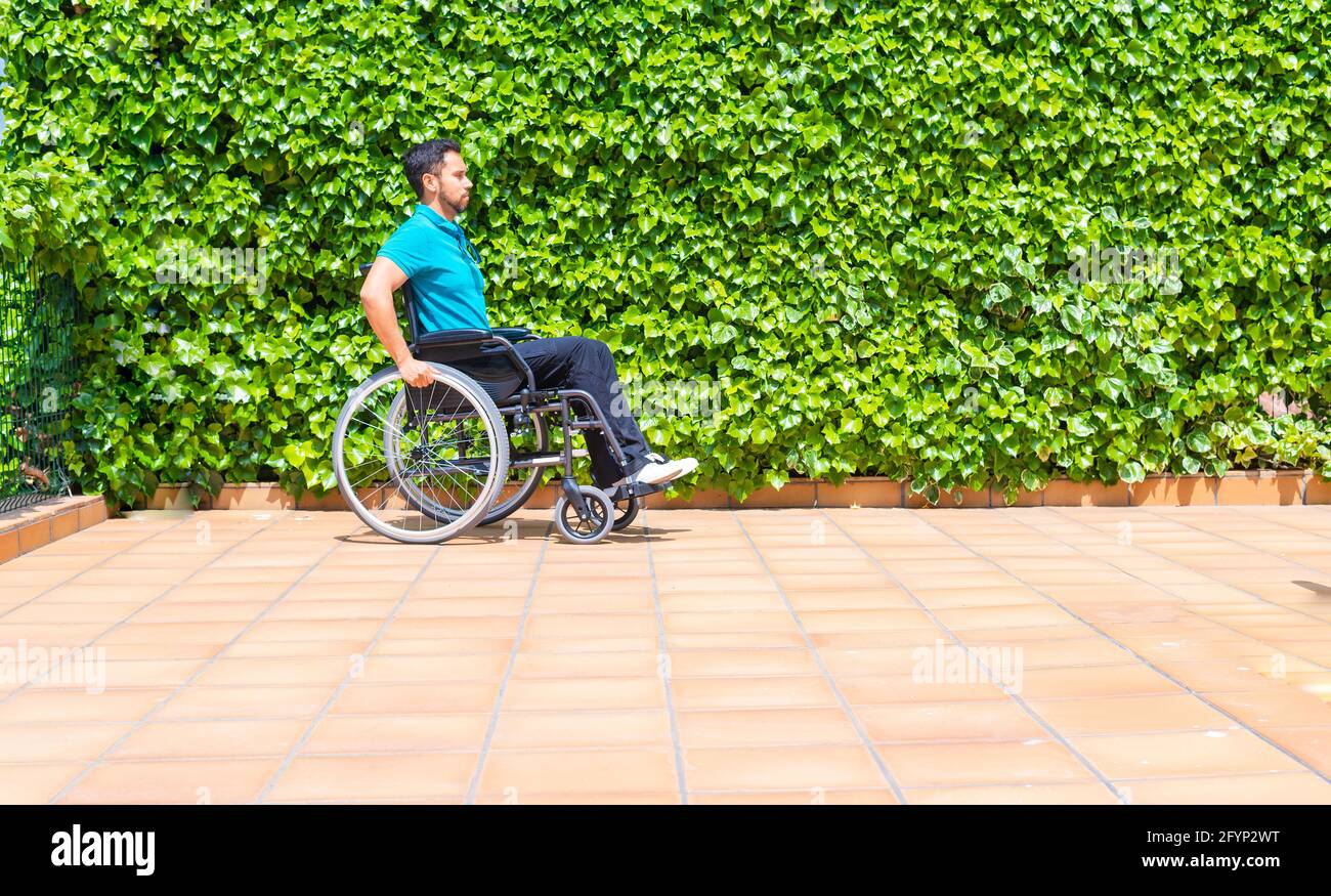 Spanish man rolling his wheelchair on tiled stone ground next to tall