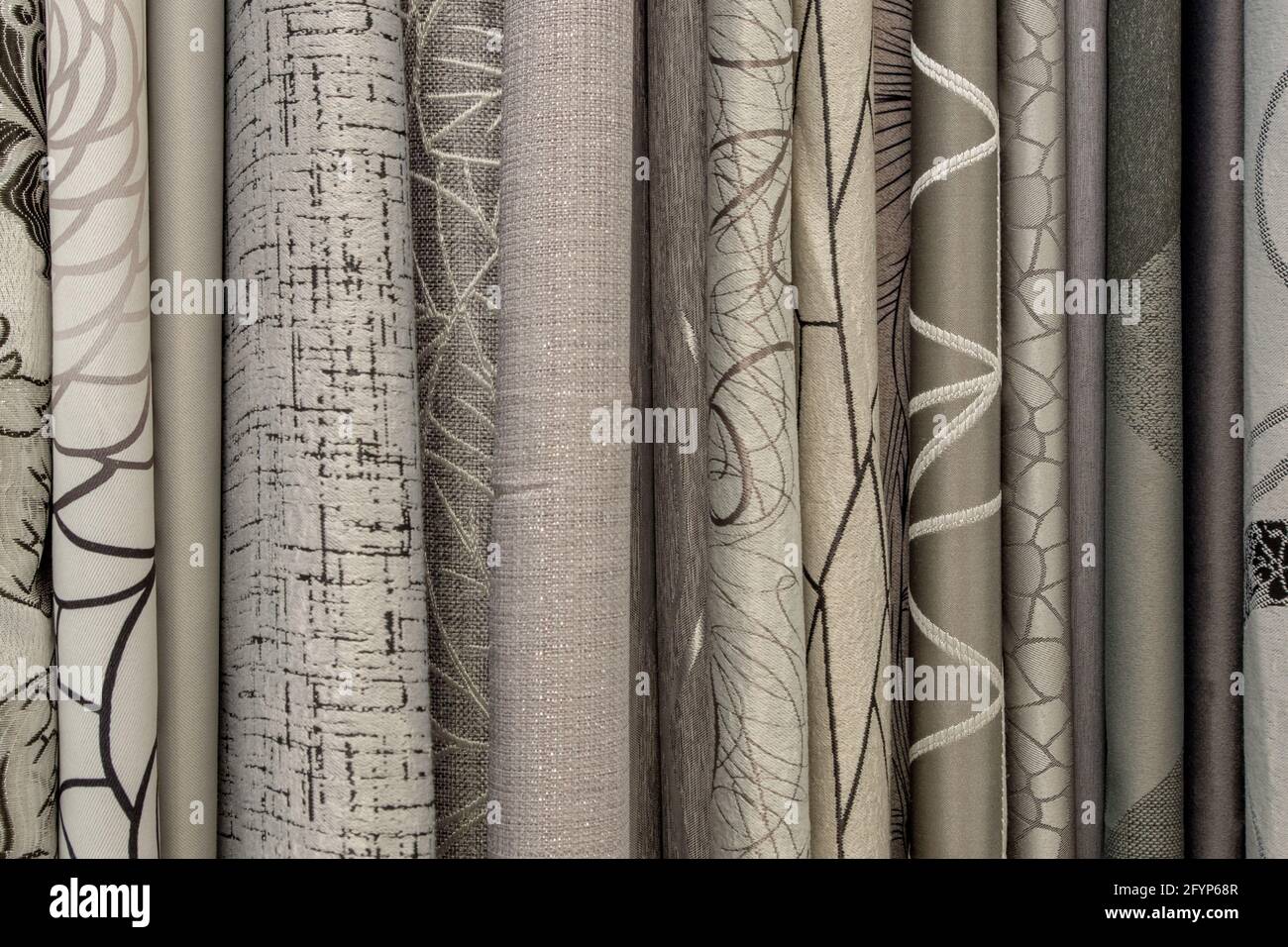 A fragment of the rounded ends of the edges hanging vertically in a row of fabric curtains in gray, beige and brown shades. Natural textile background Stock Photo