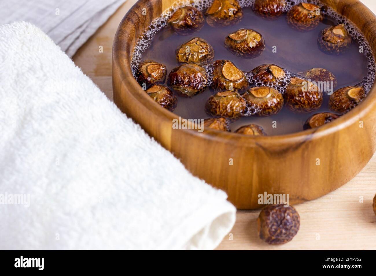 Brown dry soap nuts (Soapberries, Sapindus Mukorossi) in the water with the towel for organic laundry and gentle natural skin care on light background Stock Photo