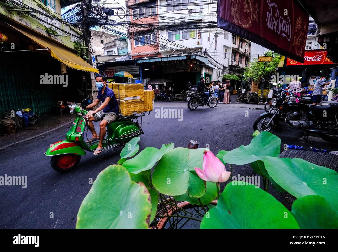 A man riding a Vespa scooter transports some boxes along a narrow road in Talat Noi, Bangkok, Thailand Stock Photo