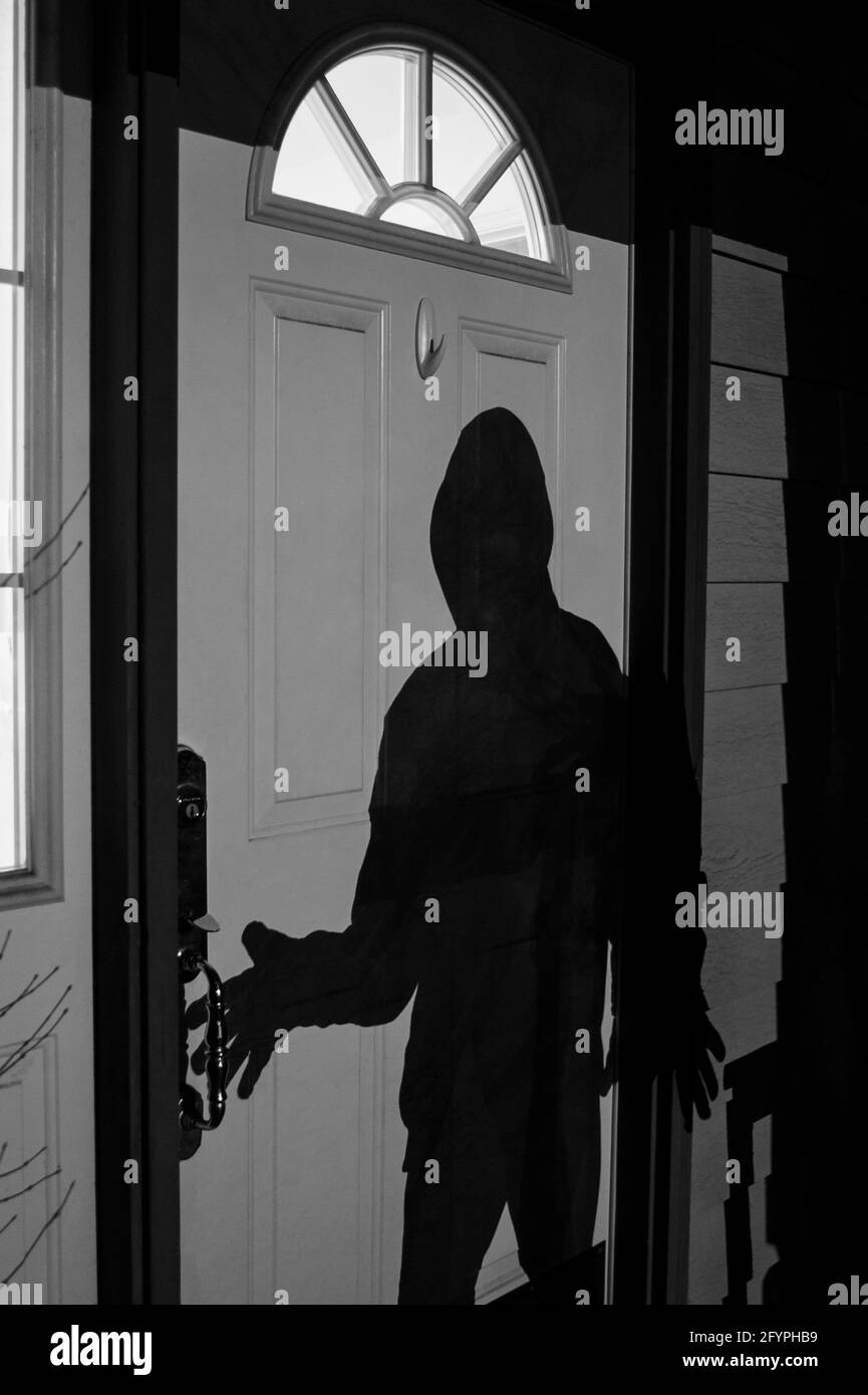 Burglar breaking into home at night standing at the front  door Stock Photo