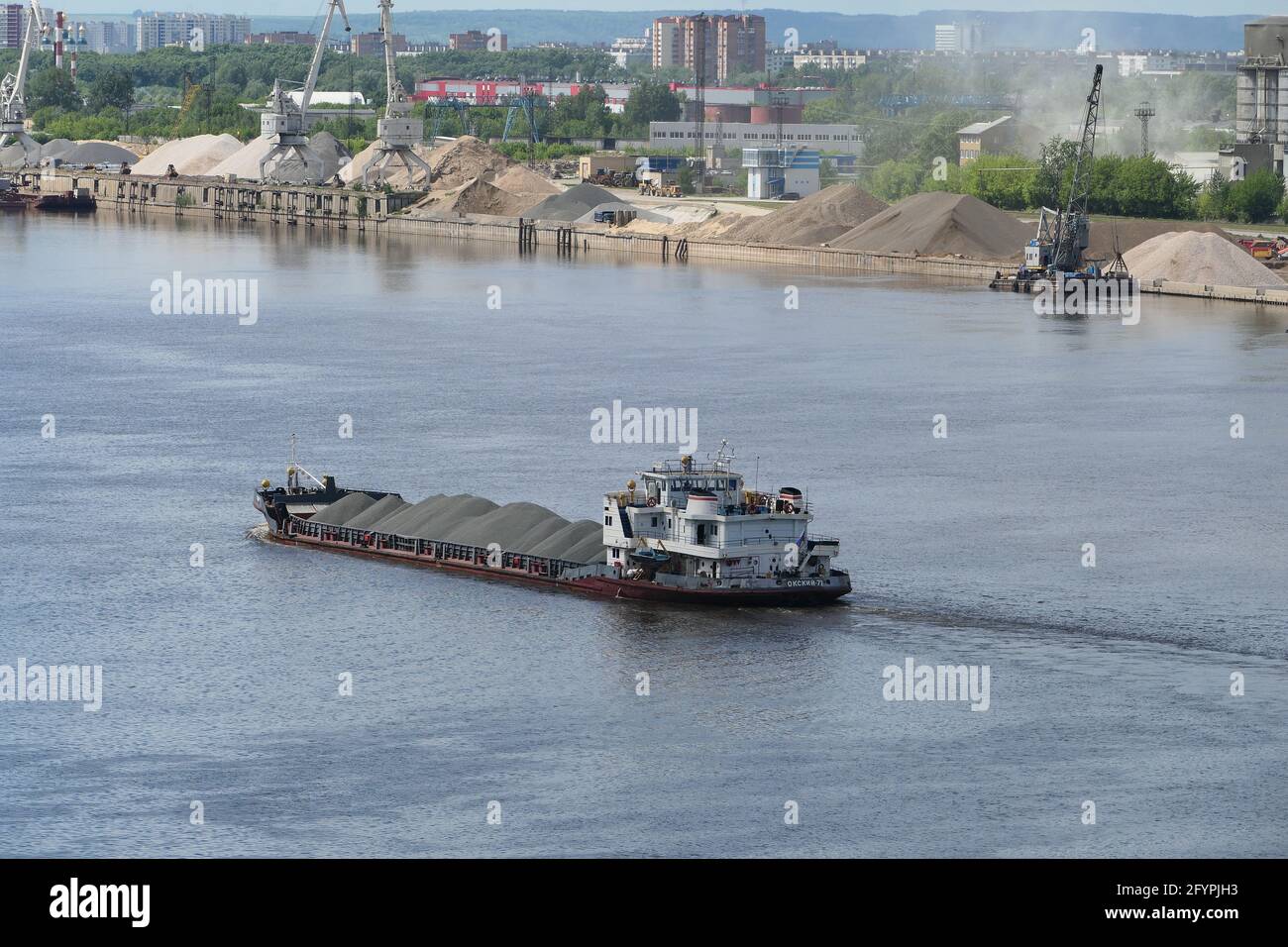 The tug transports a barge loaded with sand along the river. Stock Photo