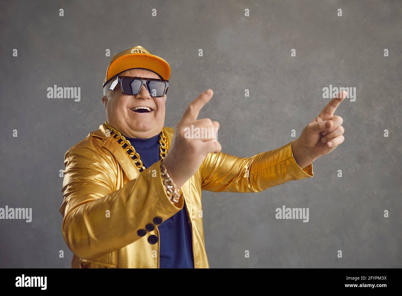 Funny senior man in golden jacket, baseball cap and chain necklace dancing and having fun Stock Photo