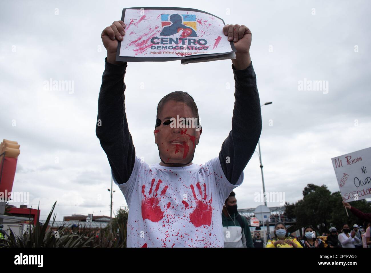 Bogota, Cundinamarca, Colombia. 28th May, 2021. a protester wears a mask of the face of President IvÃ¡n Duque, while holding a sign that reads: ''demonic center'' in reference to the Colombian political party Centro DemocrÃ¡tico on a New day of protests in BogotÃ¡ in the context of the month-long commemoration of the start of the national strike in Colombia against the Government of Ivan Duque, on March 28, 2021. Credit: Daniel Romero/LongVisual/ZUMA Wire/Alamy Live News Stock Photo
