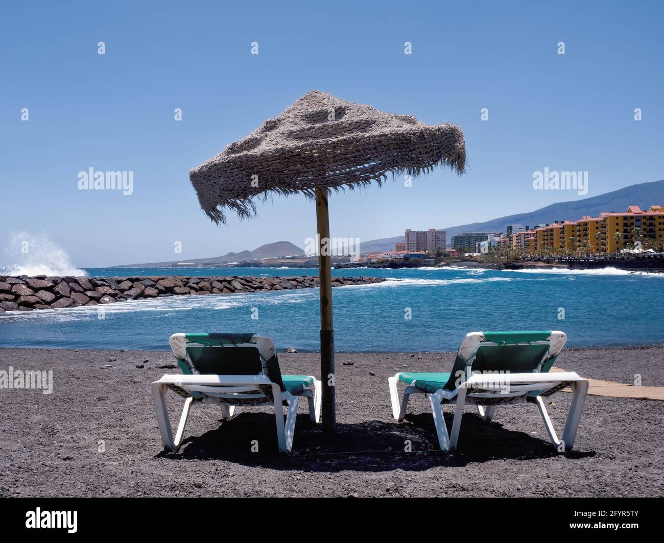 View from the lava beach over the Atlantic Ocean and the place 'Punta Larga' on the south coast of the island of Tenerife. In the foreground two empty Stock Photo