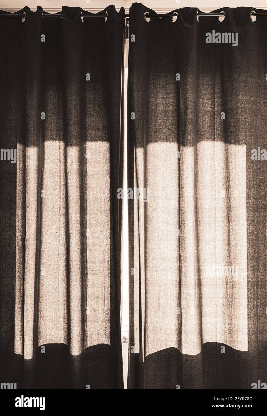 black curtain drapes closed on sunny window Stock Photo