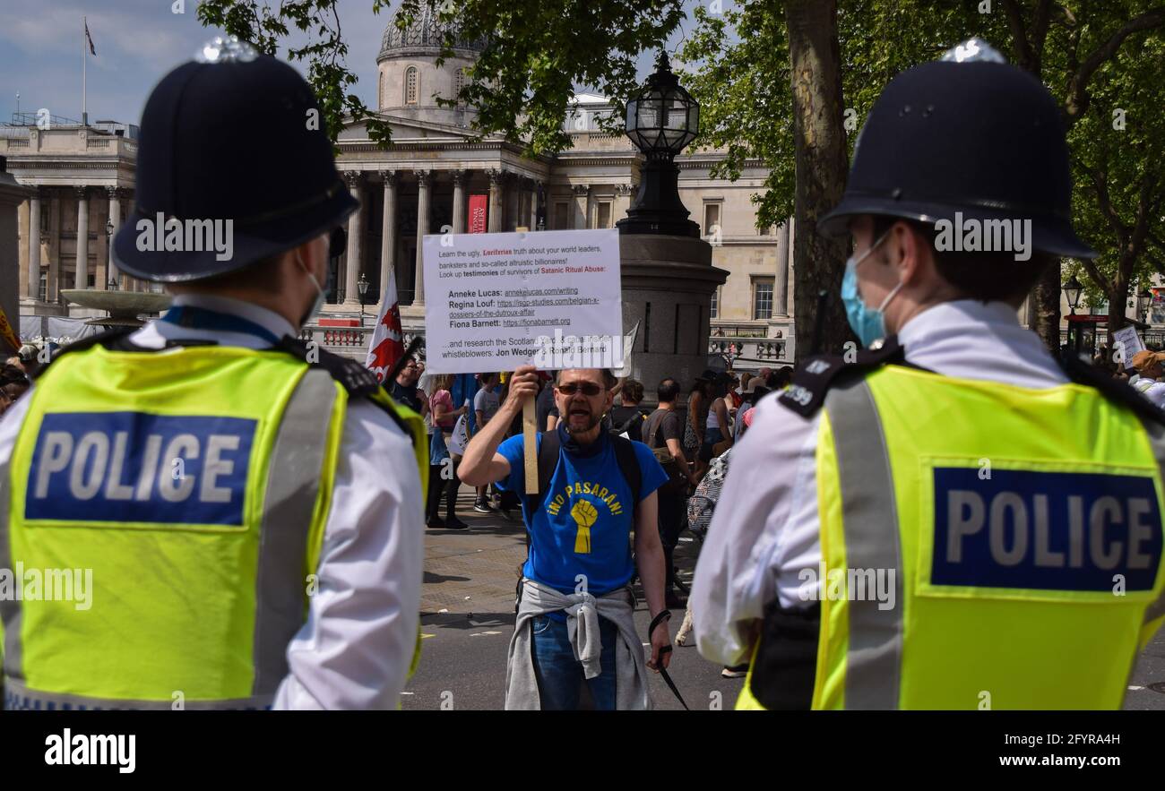 London, United Kingdom. 29th May 2021. A man holds a placard with conspiracy theories and shouts at police officers in Trafalgar Square. Thousands of people marched through Central London in protest against protective face masks, Covid-19 vaccines and lockdowns. (Credit: Vuk Valcic / Alamy Live News) Stock Photo