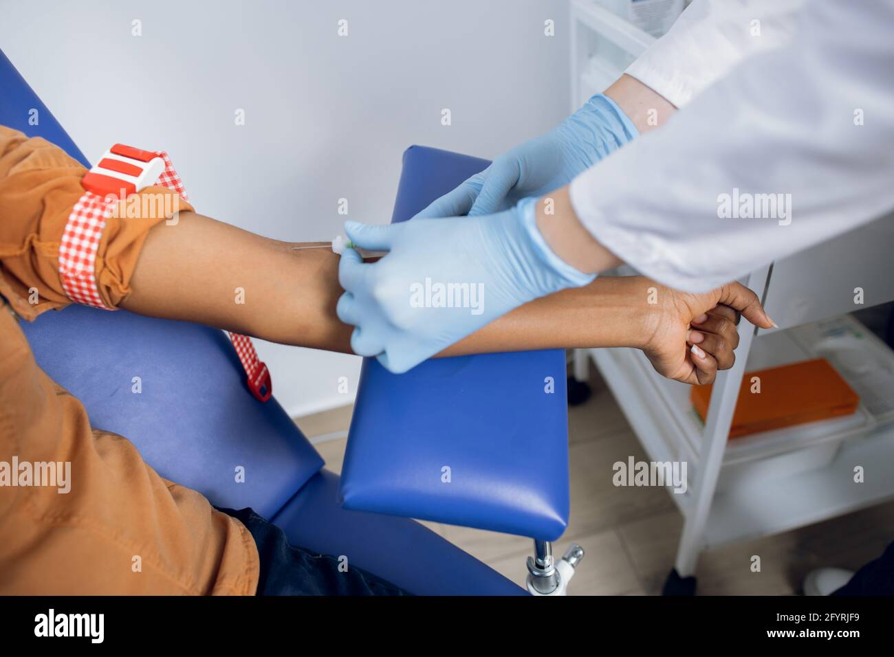 Close up cropped shot of hands of female doctor preparing patient for blood draw in modern clinic. African patient sitting on the chair and ready to have blood test Stock Photo