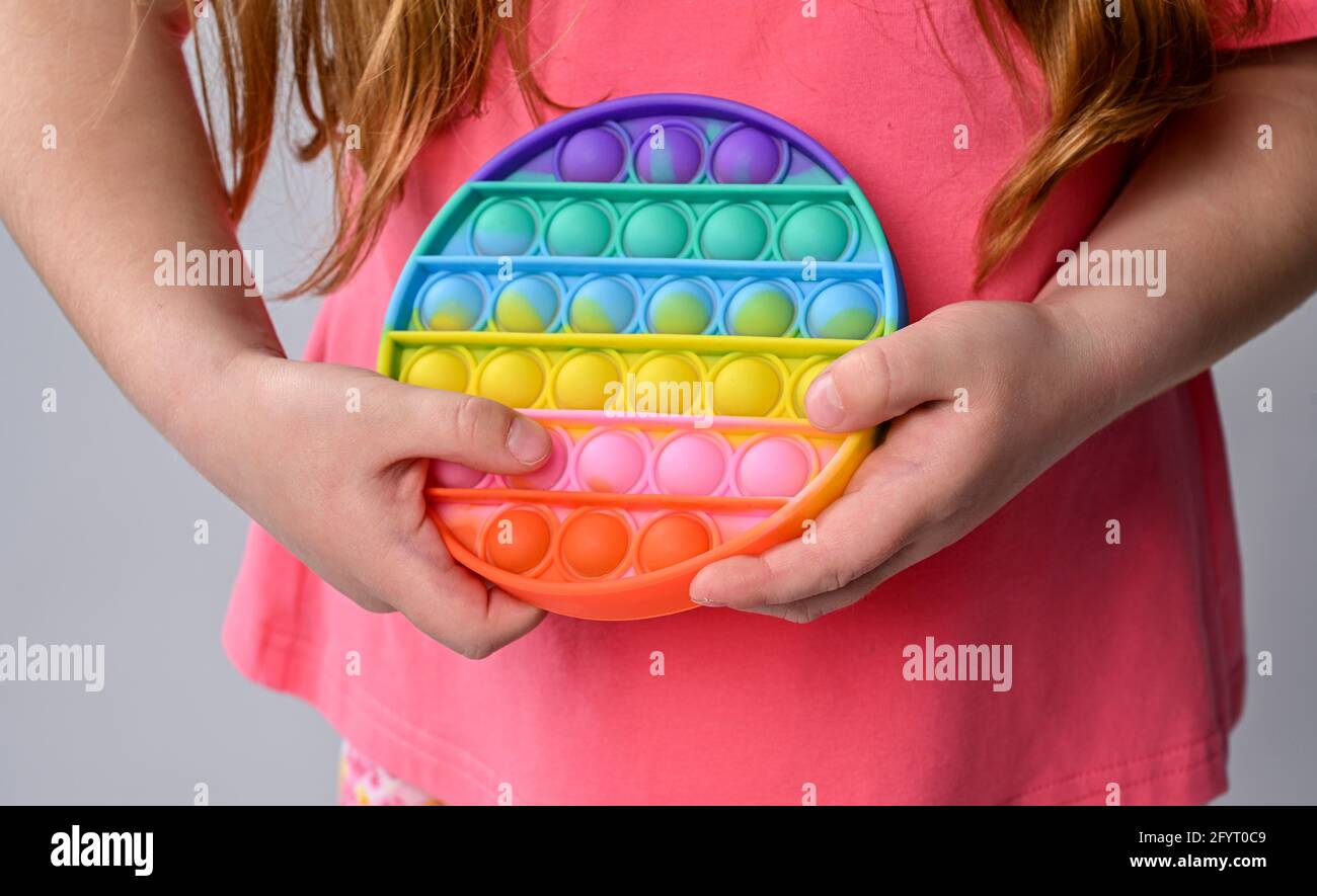Girl kid hand hold new sensory toy - pop it. Rainbow color, concave and convex bubbles. Silicone form Stock Photo