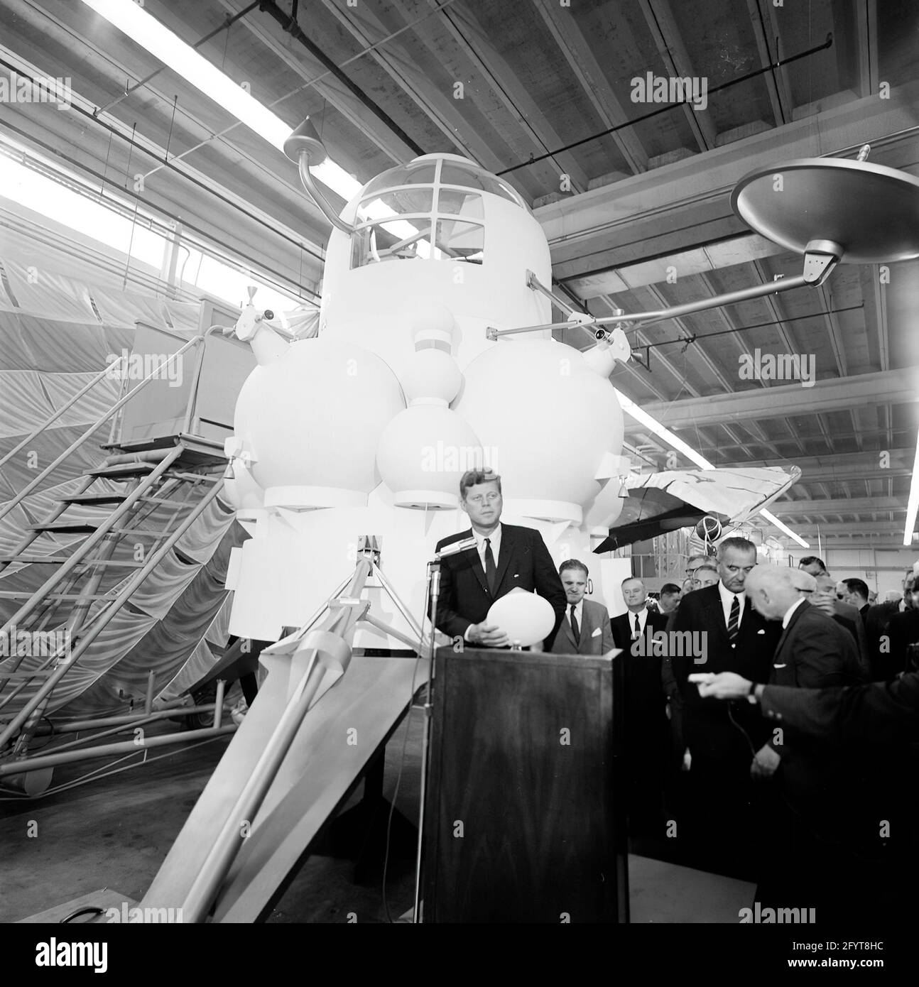 12 September 1962President John F. Kennedy (at lectern) delivers remarks, following a tour of spacecraft displays inside a hangar at the Rich Building of the Manned Spacecraft Center, Houston, Texas. President Kennedy holds a scale model of the Apollo command module, presented to him by Director of the Manned Spacecraft Center, Dr. Robert Gilruth; a mock-up of the lunar lander (also known as 'the Bug') sits in background. Standing in back: Administrator of the National Aeronautics and Space Administration (NASA), Dr. James E. Webb; Governor of Texas, Price Daniel; Director of Operations for Pr Stock Photo