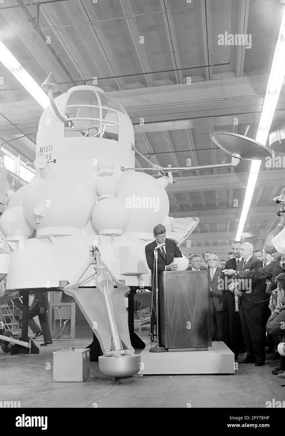 12 September 1962President John F. Kennedy (at lectern) delivers remarks, following a tour of spacecraft displays inside a hangar at the Rich Building of the Manned Spacecraft Center, Houston, Texas. President Kennedy holds a scale model of the Apollo command module, presented to him by Director of the Manned Spacecraft Center, Dr. Robert Gilruth; a mock-up of the lunar lander (also known as 'the Bug') sits at left in background. Standing in back: Director of Operations for Project Mercury, Dr. Walter C. Williams; Associate Administrator of the National Aeronautics and Space Administration Stock Photo
