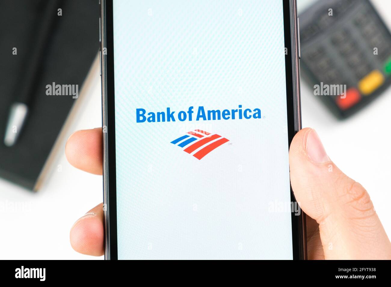 Bank of America logo on the smartphone screen in mans hand on the background of payment terminal, May 2021, San Francisco, USA Stock Photo