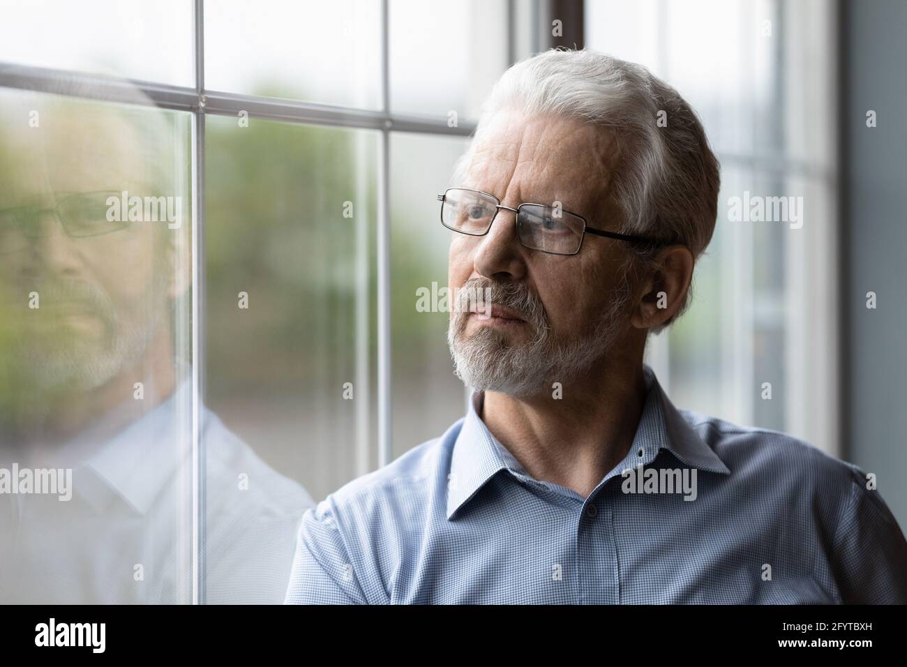 Mature thoughtful man standing indoor looking out the window Stock Photo