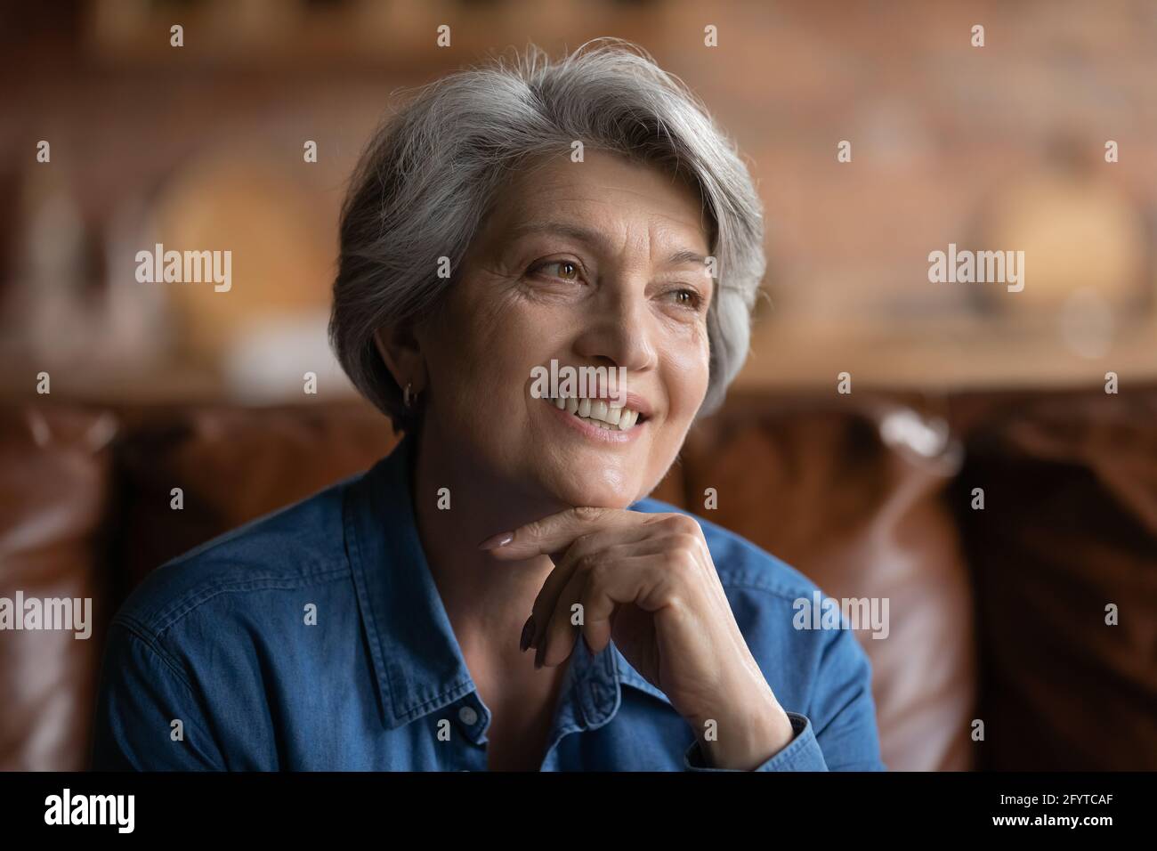 Elderly hoary female sitting on couch smiling looking away Stock Photo