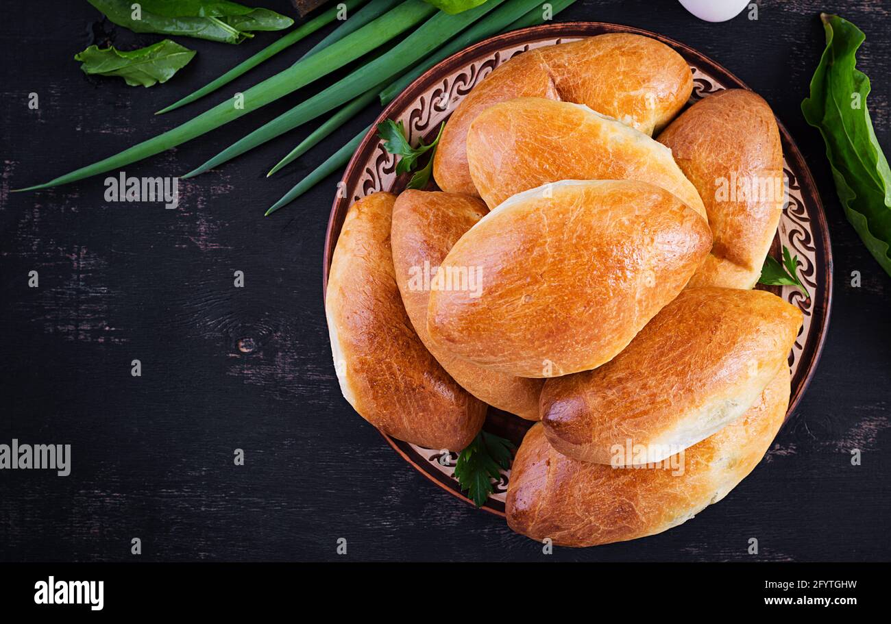 Traditional Ukrainian pies with eggs, green onion, sorrel on dark  background. Russian piroshki, homemade baked patties. Top view, above, copy space Stock Photo