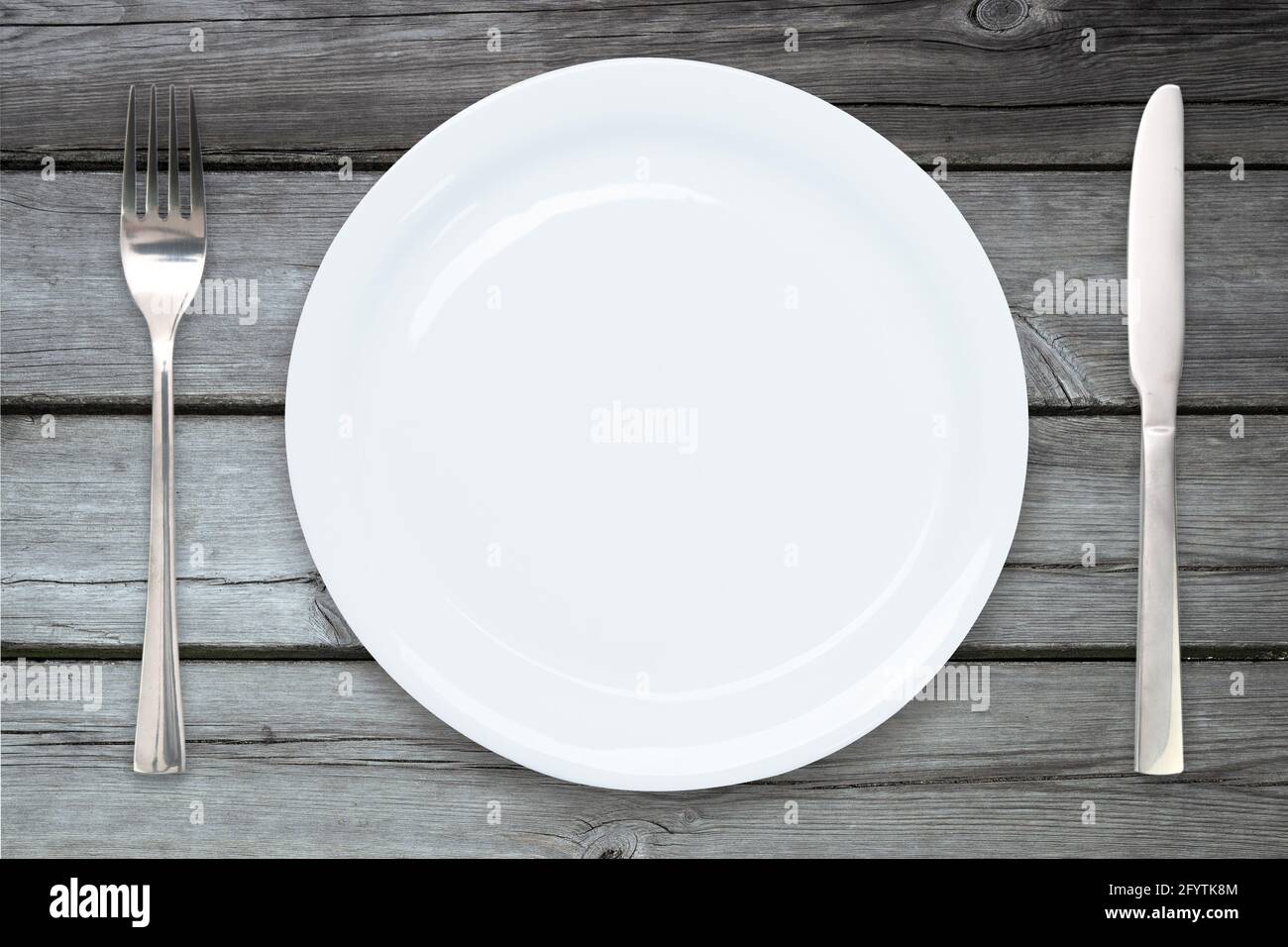 Cooking template - top view of an empty ceramic white plate with cutlery on a wooden vintage table Stock Photo