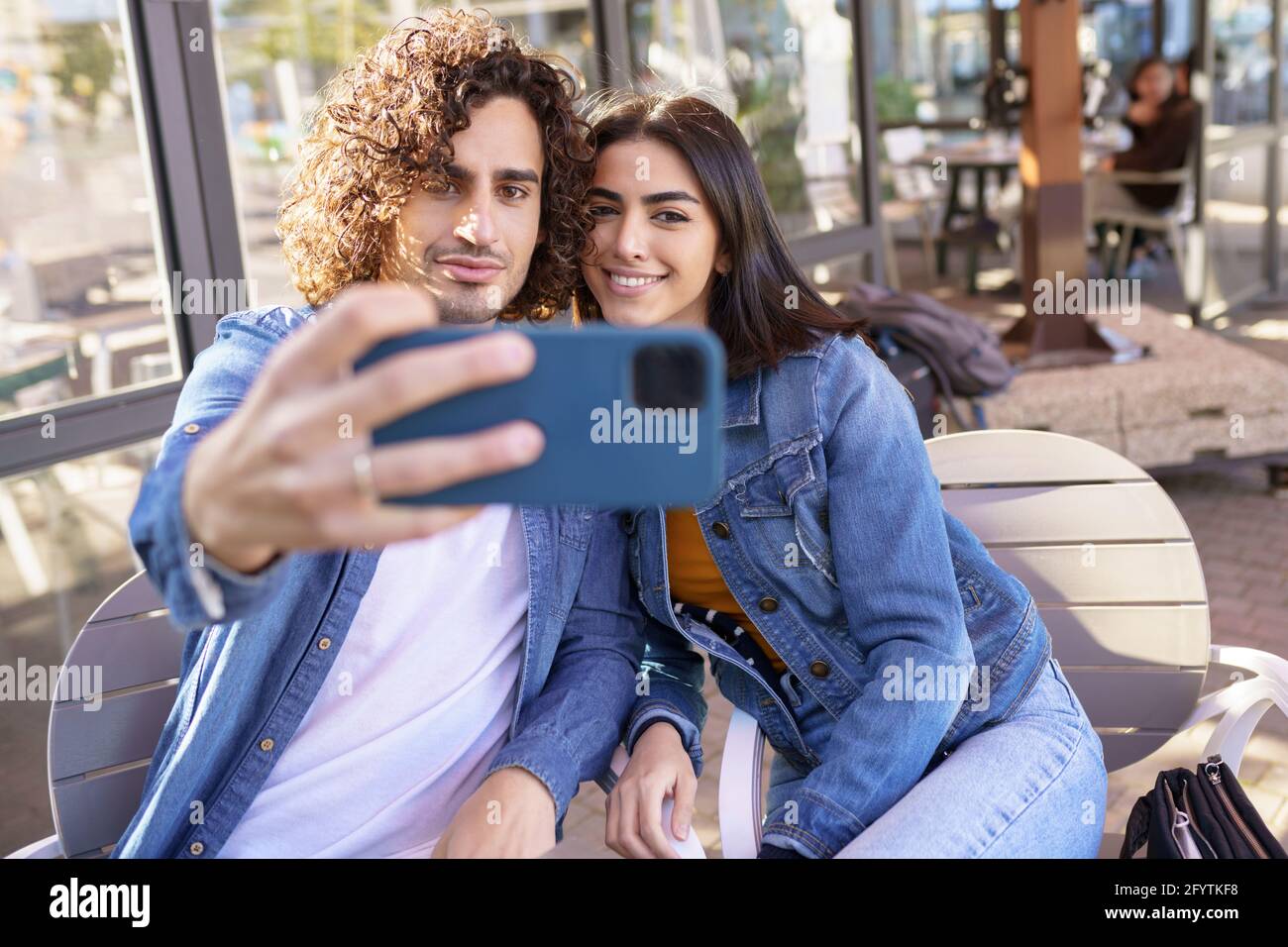 Arab couple taking selfie pictures with their smartphone, sitting on the terrace of a bar. Stock Photo
