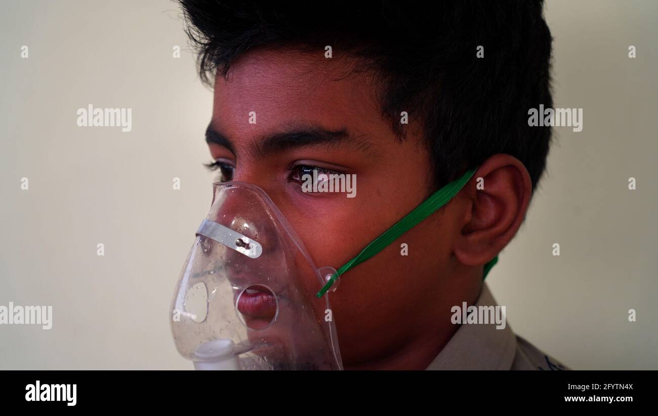 A Little boy infected with Covid 19 disease. Child Patient inhaling oxygen wearing mask at home. Indian boy taking treatment of Asthma, lungs, and cou Stock Photo
