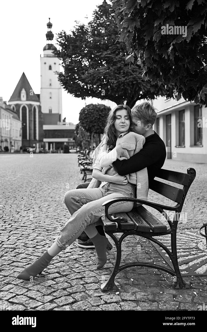 Beautiful young couple cuddling on a bench in a European town. Romatnic date and love concept. Stock Photo