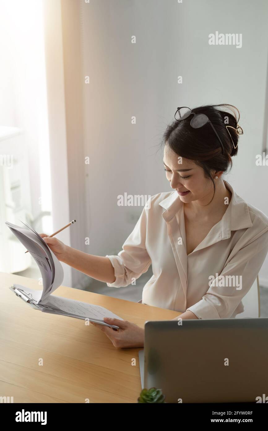 Female asian businesswoman analyzing the business report with laptop computer in the office. vertical shot Stock Photo