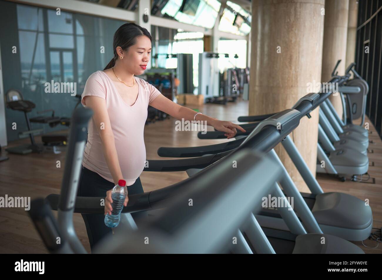 Pregnant Asian woman exercising in the gym indoors walking on a treadmill for a fit and active lifestyle during pregnancy Stock Photo