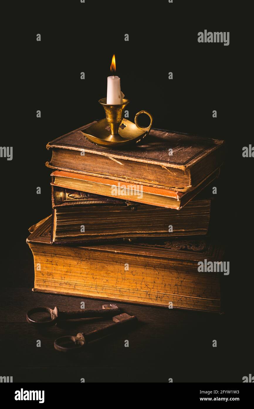 Pile of old antique books with candle and old rusty keys in vintage style on wooden black background Stock Photo