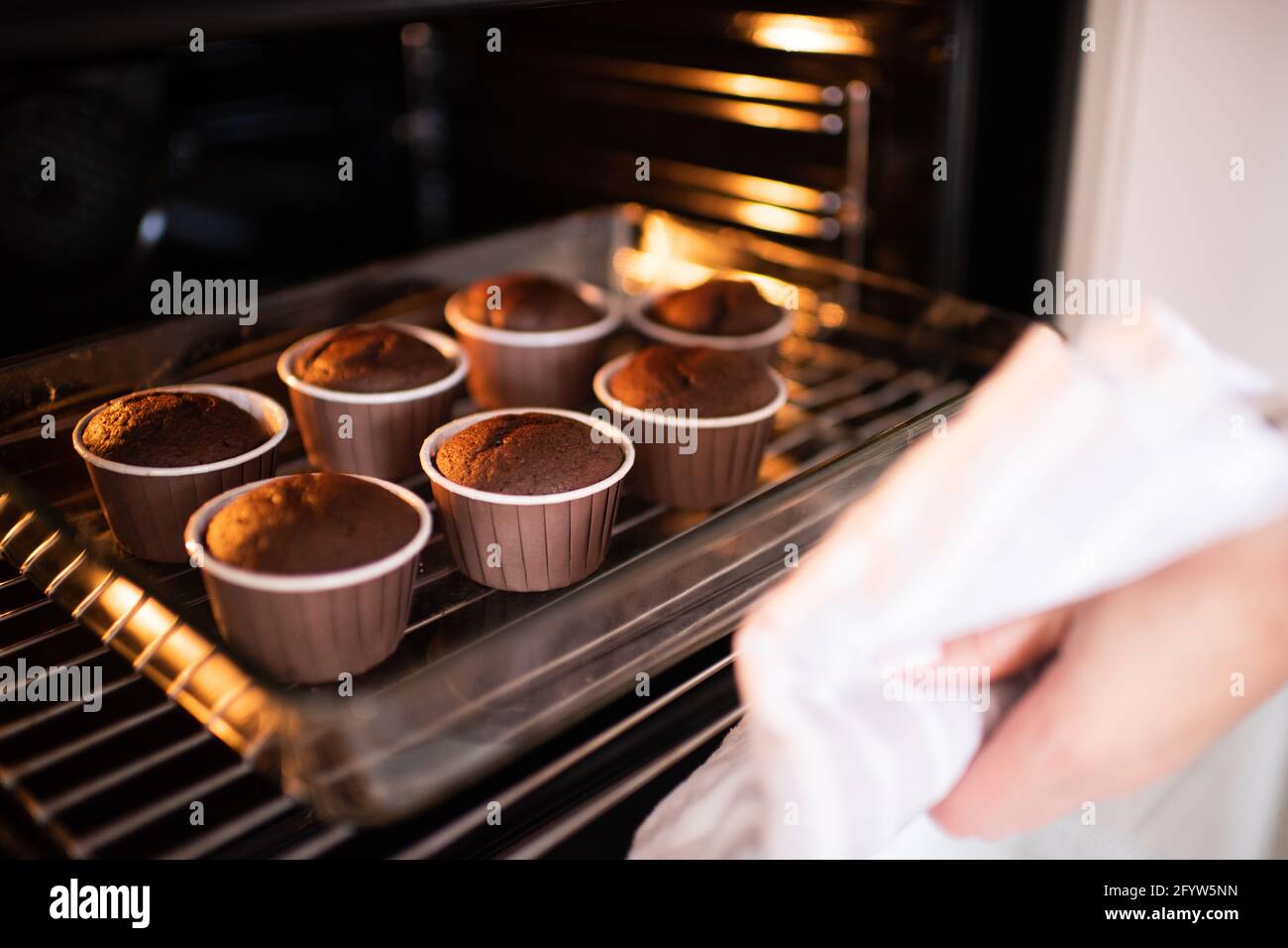 Woman baking chocolate cup cakes in glass tray in kitchen closeup. Young  girl put muffins in hot over. Female cooking tasty snack pastry at home.  Hea Stock Photo - Alamy