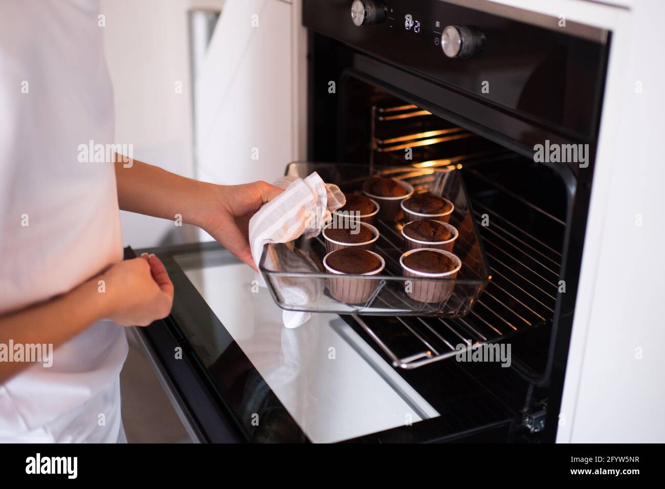 Woman baking chocolate cup cakes in glass tray in kitchen closeup. Young  girl put muffins in hot over. Female cooking tasty snack pastry at home.  Hea Stock Photo - Alamy