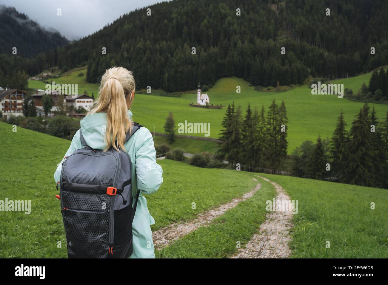 Woman with backpack on hiking trail to St. Johann church in Val di Funes valley, Dolomites, Italy, Europe Stock Photo
