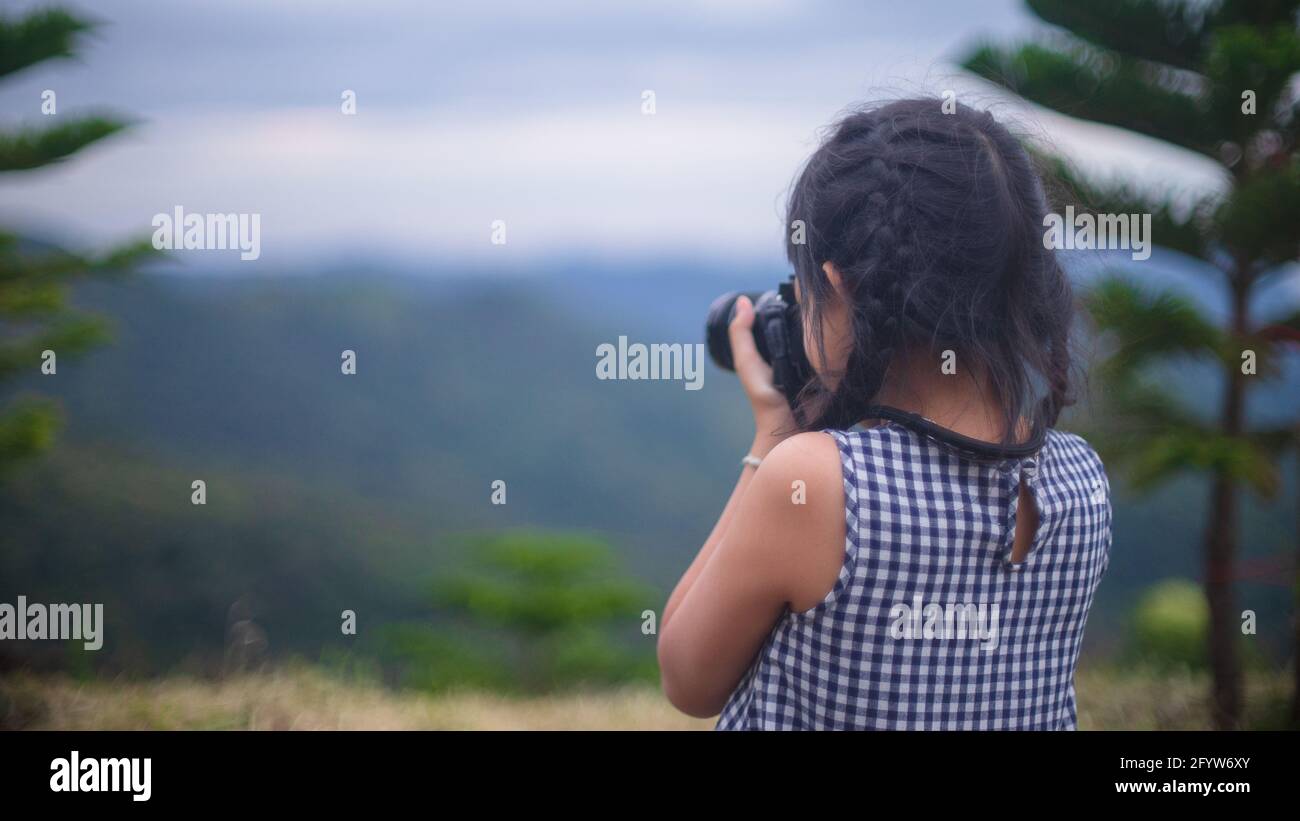 Little child girl taking photo of beautiful landscape.She standing on hill with background of mountains Stock Photo