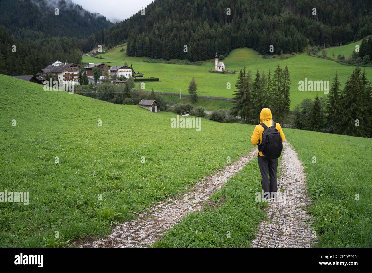 A Man with backpack hiking down the Val di Funes valley to St. Johann church, Dolomites, Italy, Europe Stock Photo