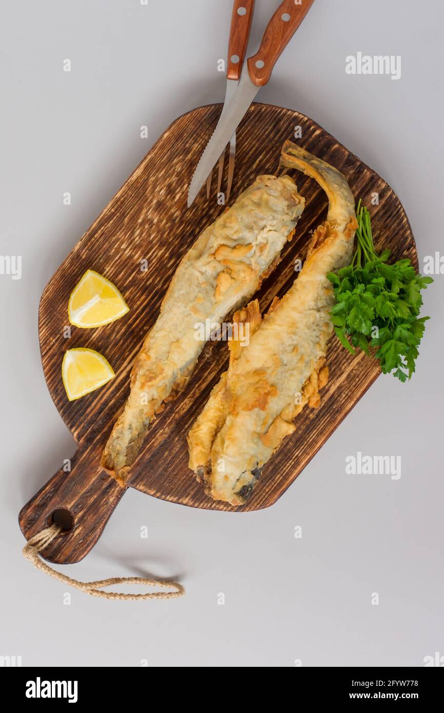 Navaga Fish Top view of fried fish navaga served on wooden cutting board with lemon ...