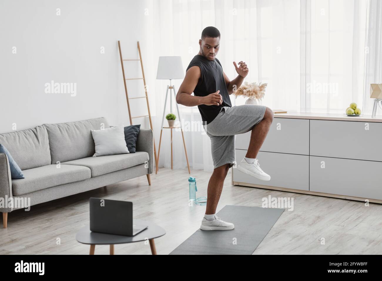 African Guy Doing Standing Knee Raise Exercise At Laptop Indoor Stock Photo Alamy