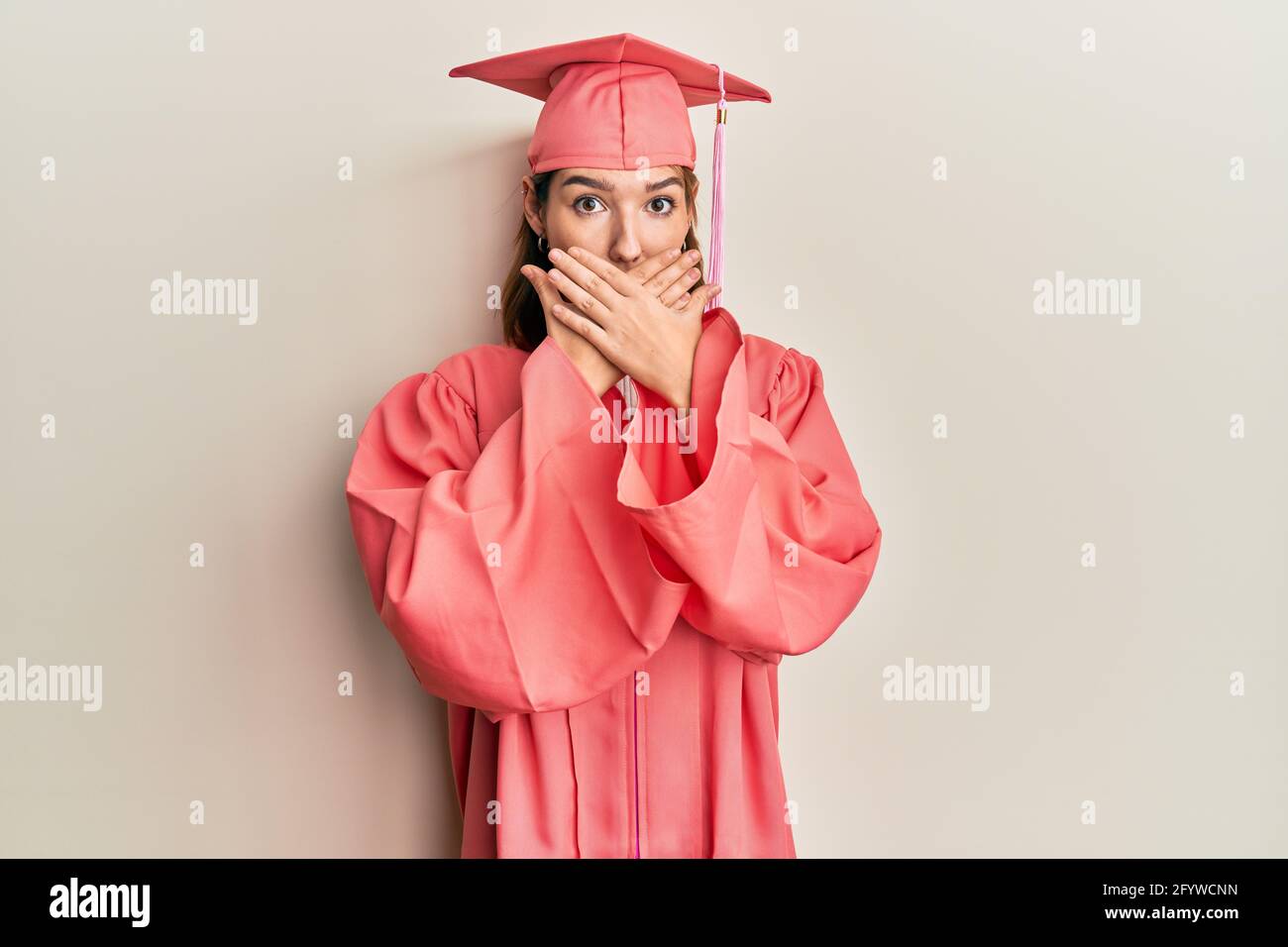 Young caucasian woman wearing graduation cap and ceremony robe shocked ...