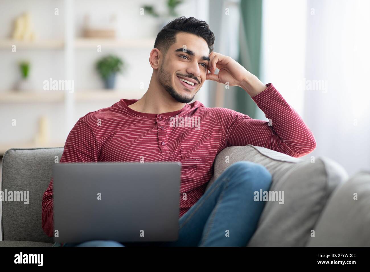 Dreamy arab guy sitting on sofa with laptop Stock Photo