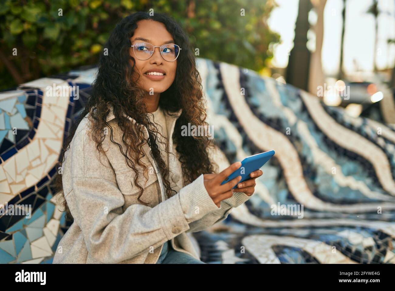 Young latin woman smiling happy using touchpad sitting on the bench at ...