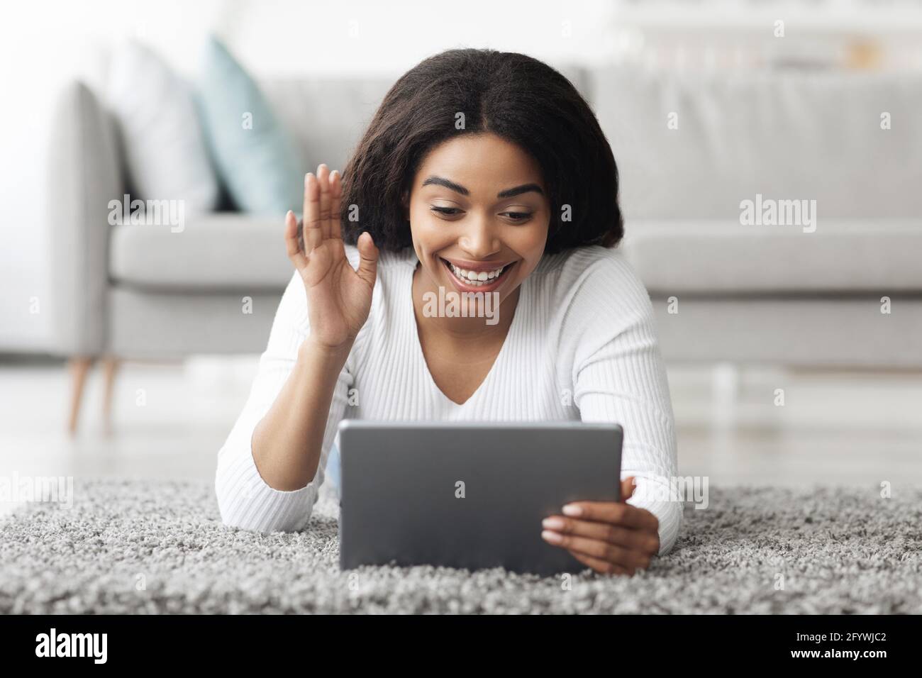 Excited black lady having video call on digital tablet, lying on ...