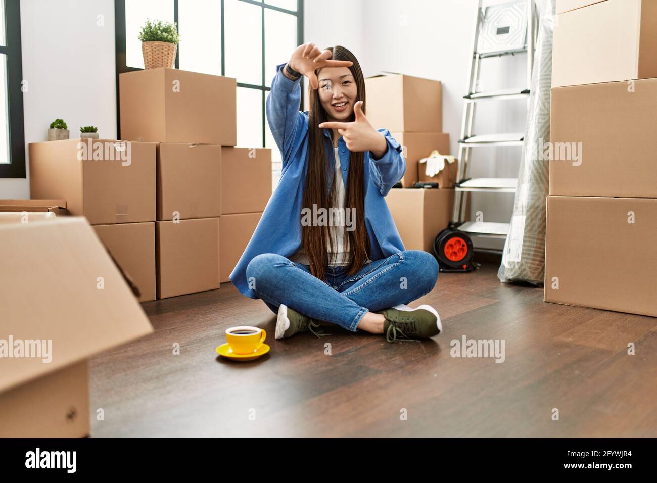 Young chinese girl sitting on the floor at new home smiling making ...