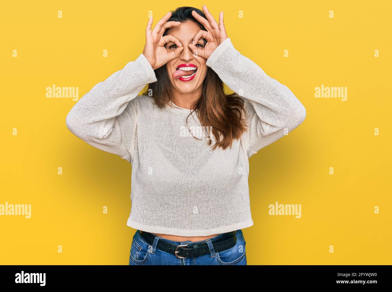 Beautiful hispanic woman wearing casual sweater doing ok gesture like  binoculars sticking tongue out, eyes looking through fingers. crazy  expression Stock Photo - Alamy