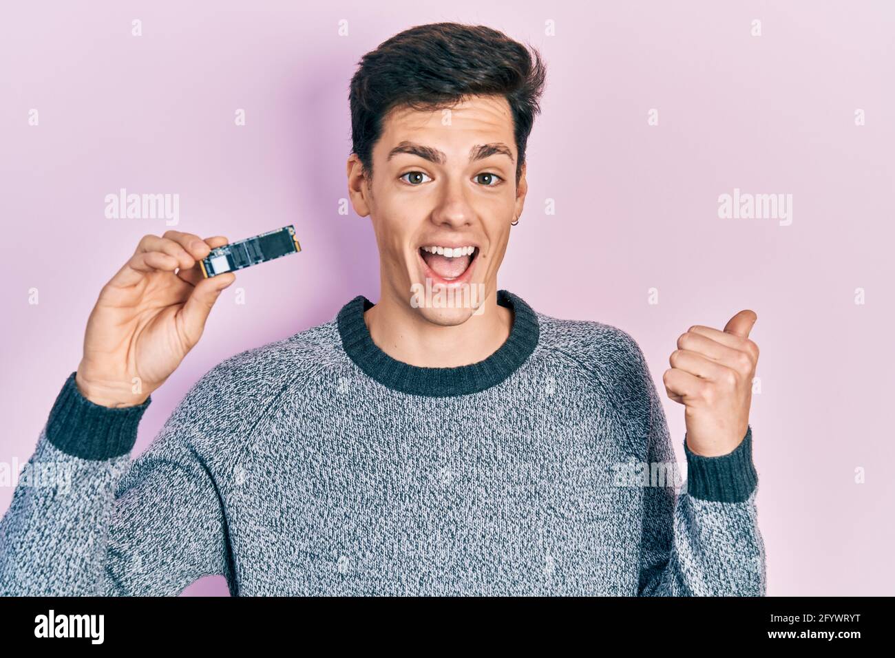 Young hispanic man holding ssd memory pointing thumb up to the side ...