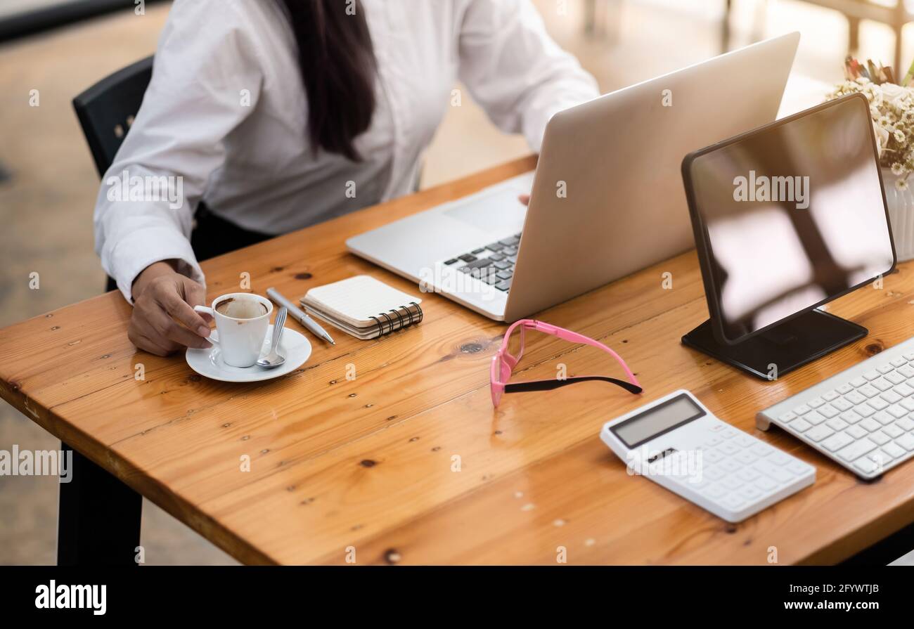 Accounting woman using laptop computer on workplace table with digital tablet and calculator at cafe Stock Photo